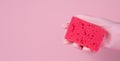 A woman\'s hand in a rubber glove holds a cleaning sponge on a pink background. Close-up. Copy space Royalty Free Stock Photo