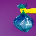 A woman`s hand in a rubber glove holds a transparent green garbage bag with empty plastic bottles.