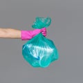 A woman`s hand in a rubber glove holds a transparent green garbage bag with empty plastic bottles.