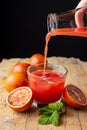 Woman`s hand serving blood orange juice in a glass on rustic table with oranges and mint, vertical black background Royalty Free Stock Photo