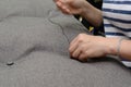 Woman`s hand sews button on the upholstery in the atelier, gray fabric, horizontal photo. Small business concept
