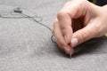 Woman`s hand sews with a needle in atelier, gray fabric, horizontal photo. Small business concept