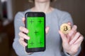 Woman`s hand showing green screen on smart phone and golden bitcoin coin Royalty Free Stock Photo