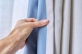 Woman& x27;s hand showing light gray curtain on blue opaque lining, fabric blackout