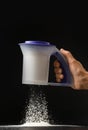 A woman's hand sifts flour through an eco-plastic sieve on a black background