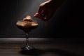 A woman`s hand with a spoon takes jelly coffee with milk in a glass bowl, which is sprinkled with chocolate chips. Deep shadows.