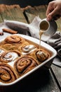 Woman`s hand spreading vanilla icing freshly baked cinnamon rolls, Cinnabon, vertical image. top view. place for text