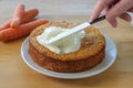 Woman`s hand spreads frosting on a baked carrot cake, wooden table