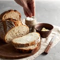Woman`s hand sprinkling sugar artisan sliced toast bread with butter on wooden cutting board. Simple breakfast Royalty Free Stock Photo