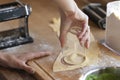 Woman`s hand stands out with a small water glass for dumplings from dough rounds on a wooden board