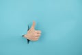 A woman's hand sticking out of a hole from a blue background shows a thumbs up. Royalty Free Stock Photo