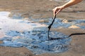 A woman`s hand stirring liquid asphalt with a wooden stick at Pitch Lake, La Brea, Trinidad island, Trinidad and Tobago