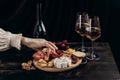 Woman`s hand takes crackers from the Appetizers board with assorted cheese, meat, sausage rosette, grape and cookies