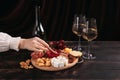 Woman`s hand takes a piece of cheese from the Appetizers board with assorted cheese, meat, sausage rosette, grape and cookies