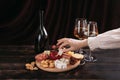 Woman`s hand takes a piece of cheese from the Appetizers board with assorted cheese, meat, sausage rosette, grape and cookies