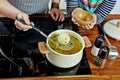 Woman`s hand taking away a boiled onion with a steel turner. Opened white saucepan on the black stove. Cooking a chicken noodle