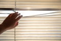 Woman's hand taking a peak through the window blinds.