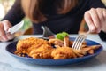 A woman`s hand using knife and fork to eat fried chicken and french fries in restaurant