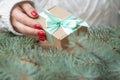 Woman`s hand in white knitted sweater with red nail polish holds a gift with a mint bow near branches of Christmas tree Royalty Free Stock Photo