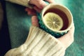 Woman`s hand in woolen sweater holding cup of tea with lemon on a cold day. Copy space. Winter and Christmas holidays Royalty Free Stock Photo