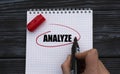 A woman`s hand writes on a white sheet the word ANALYZE on a black wooden background Royalty Free Stock Photo