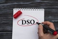 A woman`s hand writes on a white sheet the word DSO on a black wooden background Royalty Free Stock Photo