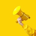 A woman`s hand in yellow clothing holds a yellow megaphone on a yellow background. alarm