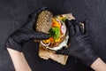 Woman`s hands in black rubber gloves are holding juicy black bun burger