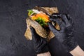 Woman`s hands in black rubber gloves are holding juicy black bun burger