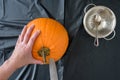 WomanÃ¢â¬â¢s hands caving fresh pumpkin on a plastic covered table, knife, spoon, and bowl