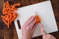 WomanÃ¢â¬â¢s hands chopping baby carrots, white cutting board on wood butcher block