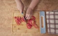 Woman`s hands chopping tomato slices with a blue knife on a wooden board at the kitchen counter Royalty Free Stock Photo