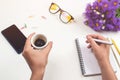 Woman`s hands with coffee on office desk. Workplace with notebook, phone, glasses, pen, lilac flowers, cup of coffee. Flat lay, t Royalty Free Stock Photo