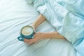 Woman`s hands from coverlet in the bed hold coffee, cannot wake up in the morning and go to work. difficult, hard monday Royalty Free Stock Photo