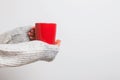Woman`s hands in cozy sweater holding a red cup of coffee, tea or hot chocolate against white wall. Royalty Free Stock Photo