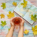 Woman`s hands with cup of tea, maple leaves and world map on the wooden background Royalty Free Stock Photo