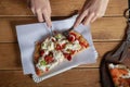 Woman`s hands cut a piece of pizza on a wooden table. Italian pizza is eaten with a fork and knife. Foreground Royalty Free Stock Photo