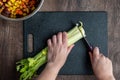 WomanÃ¢â¬â¢s hands cutting a bunch of celery, black cutting board and chef knife, bowls of diced rainbow carrots Royalty Free Stock Photo