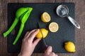 WomanÃ¢â¬â¢s hands cutting a lemon on a black cutting board, green citrus squeezer, measuring cup Royalty Free Stock Photo