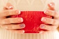 Woman& x27;s hands with french manicure and candy cane pattern on the nails. Woman with beautiful manicure holding big red Royalty Free Stock Photo