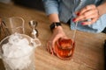 Woman`s hands gently mix cocktail in glass with long bar spoon.