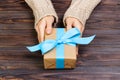 Woman`s hands give wrapped valentine holiday handmade present in craft paper with blue ribbon. Present box, decoration of gift on Royalty Free Stock Photo