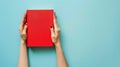 Woman\'s hands hold book with blank red cover, light blue background. Ai Generated Royalty Free Stock Photo