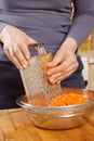 The woman`s hands hold the carrot and rub it on the kitchen grater.