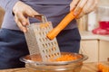 Female hands hold a raw carrot and grind it into small pieces on a metal kitchen grater.