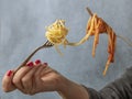 A woman`s hands hold two forks with spaghetti in white on one side and spaghetti with tomato sauce on the other