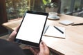 A woman`s hands holding black tablet pc with white blank screen with notebook and coffee cup on table Royalty Free Stock Photo