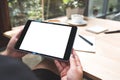 A woman`s hands holding black tablet pc with white blank screen with notebook and coffee cup on table Royalty Free Stock Photo