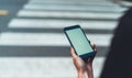 Woman`s hands holding close up mobile phone with blank white screen in city on background crosswalk city