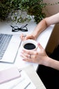 Woman`s hands holding cup of coffee in cozy office with laptop and green plants Royalty Free Stock Photo